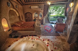 Una habitación con cama, zona de estar, bañera con pétalos de rosa y vistas al exterior.