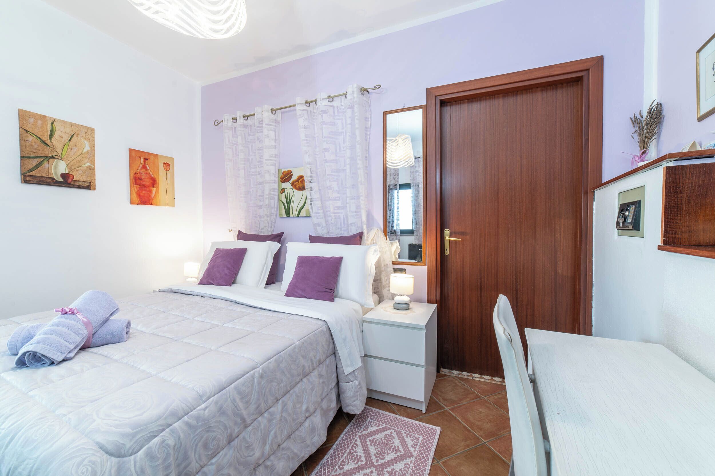 Un dormitorio con cama, mesitas de noche, una silla y una puerta.
