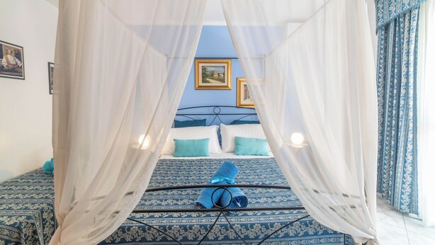 A bedroom with a canopy bed, blue patterned bedding, and a neatly folded towel on the bed.