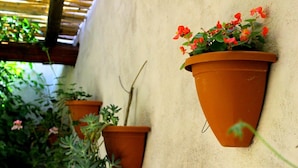 Terracotta hanging planters with plants and flowers against a wall.
