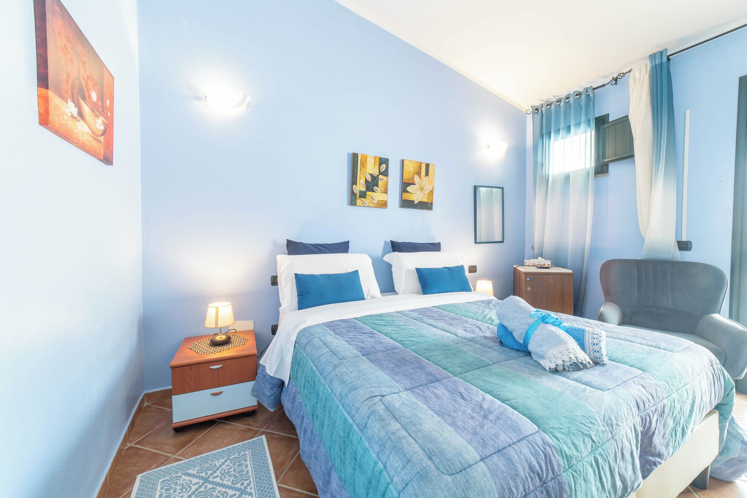 Un dormitorio con cama, mesitas de noche, una silla y obras de arte en la pared.