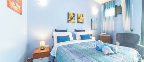 Un dormitorio con cama, mesitas de noche, una silla y obras de arte en la pared.