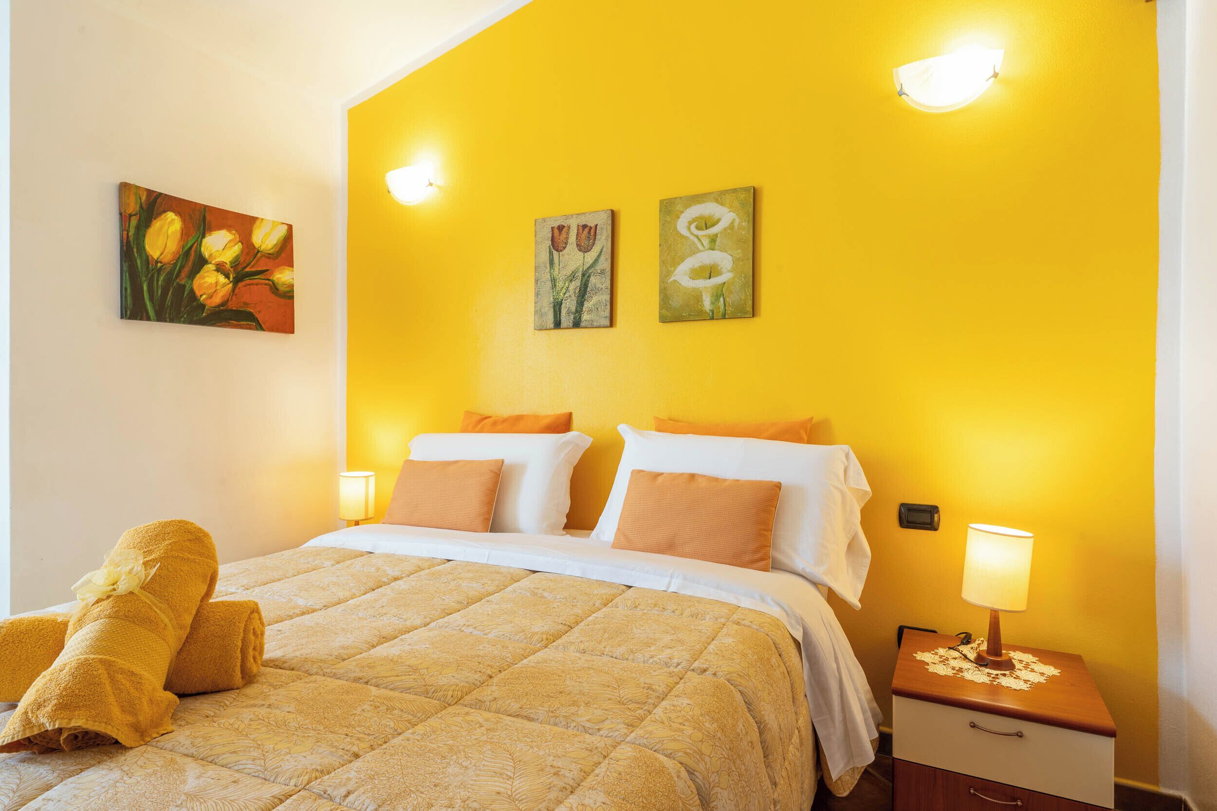 A hotel room with a bed, a nightstand, a lamp, and two paintings on the wall.