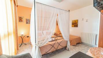 A bedroom with a four-poster bed, a bedside table, a lamp, and a radiator.