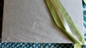 A package with a green ribbon and a label, placed on a patterned fabric.