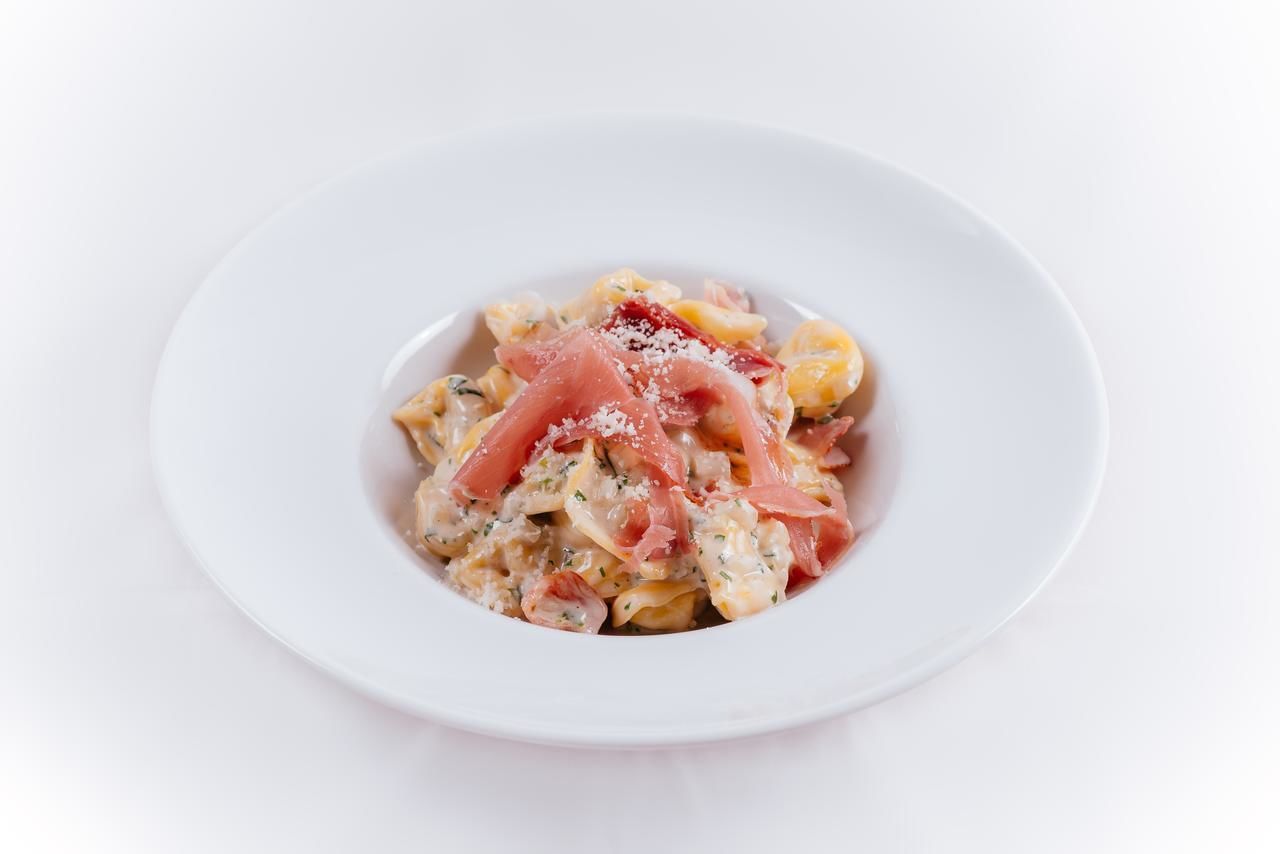 A white plate with pasta and prosciutto.