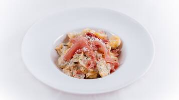 A white plate with pasta and prosciutto.
