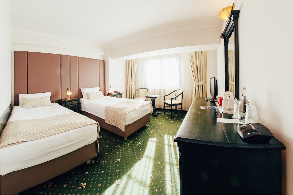 Une chambre d’hôtel avec deux lits, un bureau, une chaise, un miroir et une fenêtre avec des rideaux.