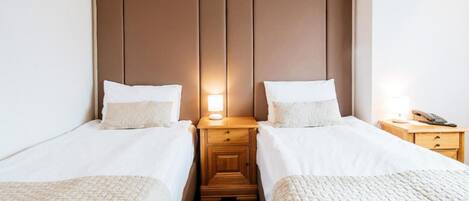 Una habitación de hotel con dos camas individuales, una mesita de noche de madera con lámpara y un suelo estampado.