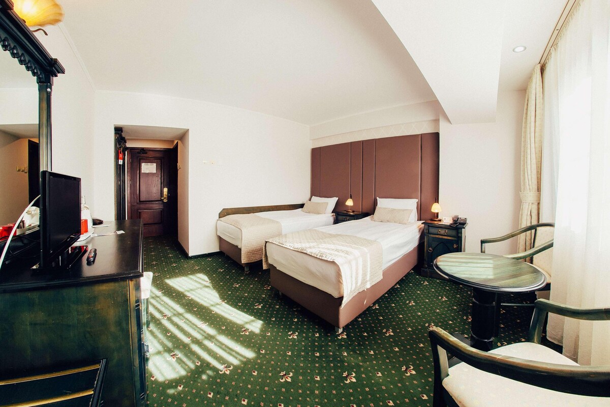 A hotel room with a large bed, a desk with a computer, and a chair.