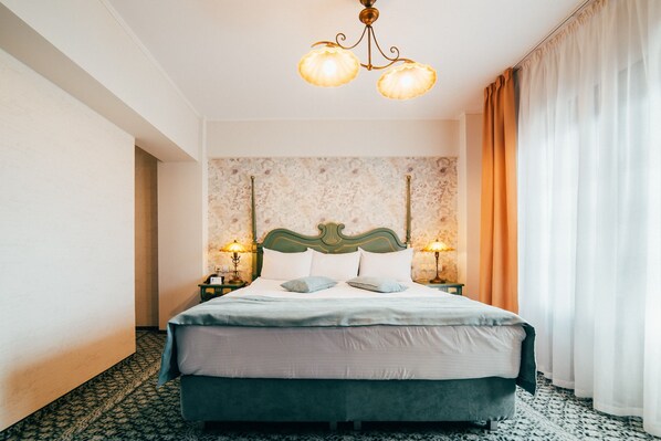 Quarto de hotel com uma cama grande, duas luminárias de cabeceira, papel de parede estampado e um lustre.