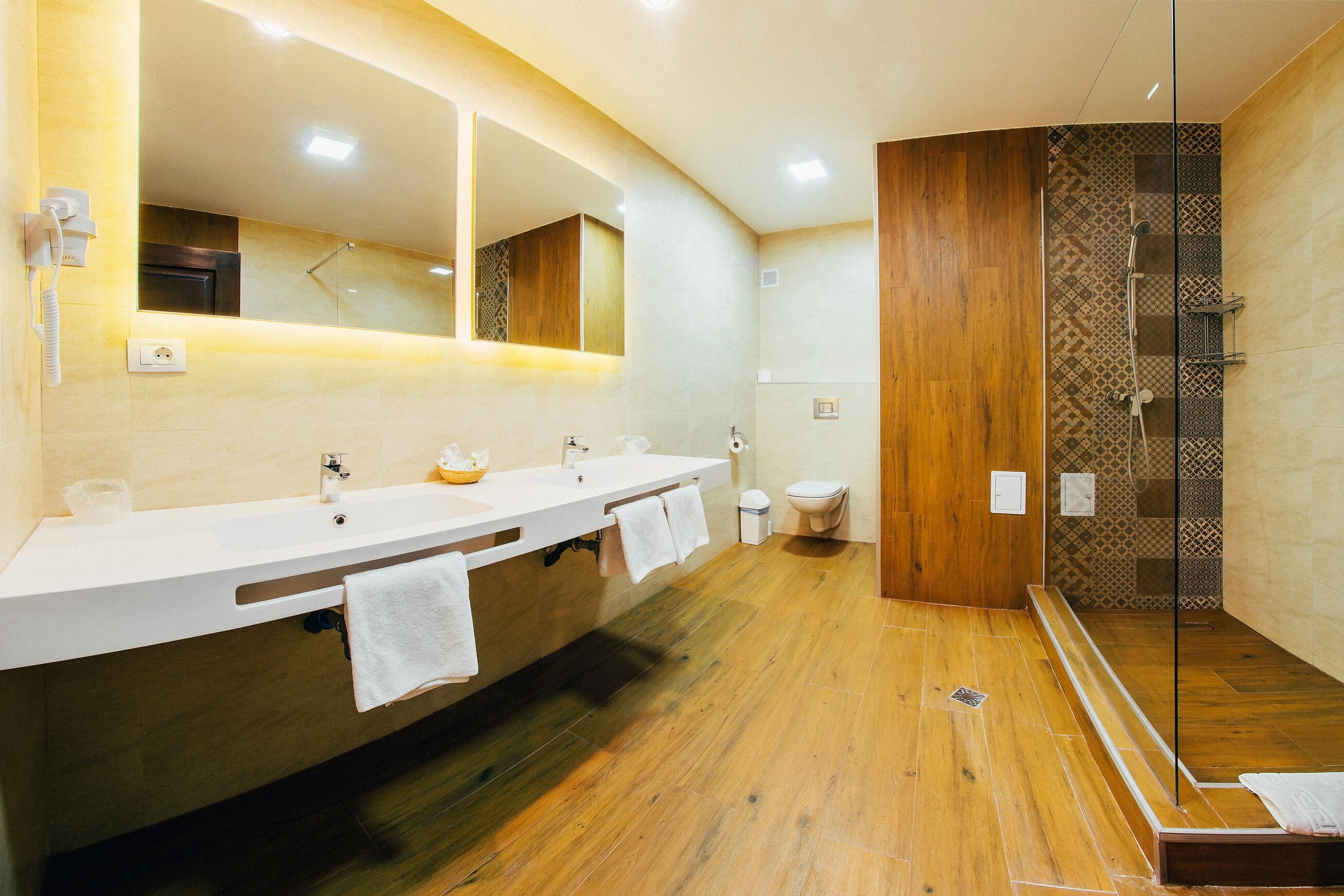 A modern bathroom with a wooden floor, two sinks, a large mirror, and a glass-enclosed shower area.