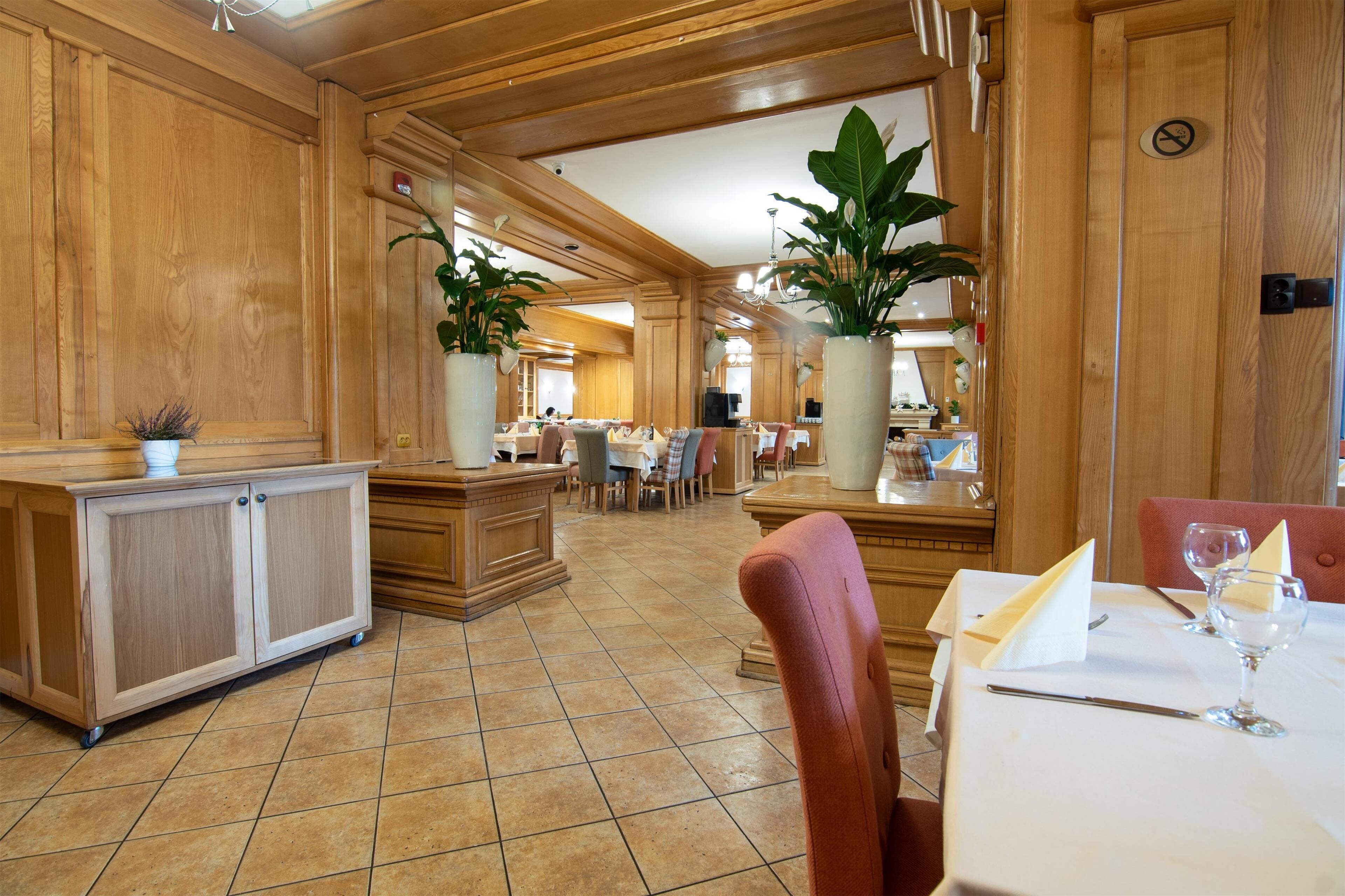 A spacious hotel lobby with wooden paneling, a reception desk, and a dining area with tables and chairs.