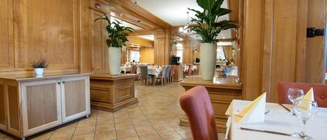A spacious hotel lobby with wooden paneling, a reception desk, and a dining area with tables and chairs.