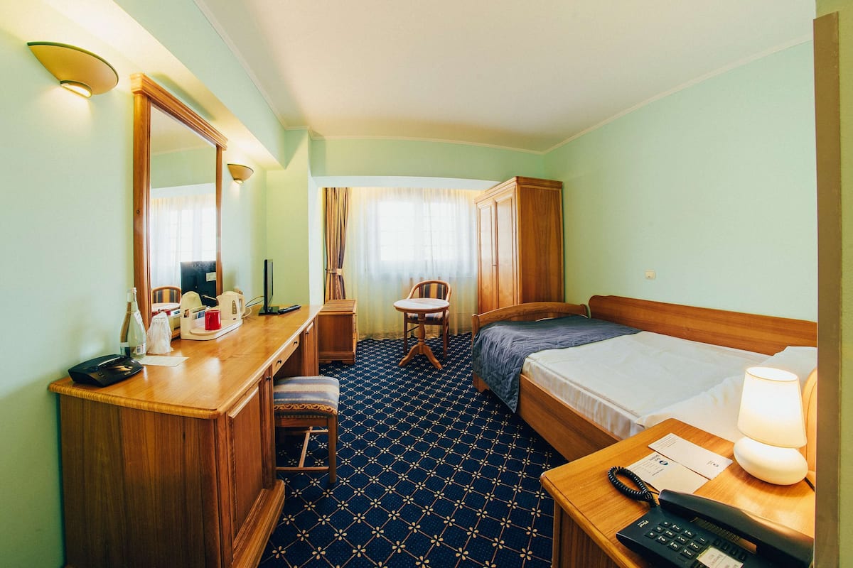 A hotel room with a bed, a desk with a telephone, a chair, and a mirror.
