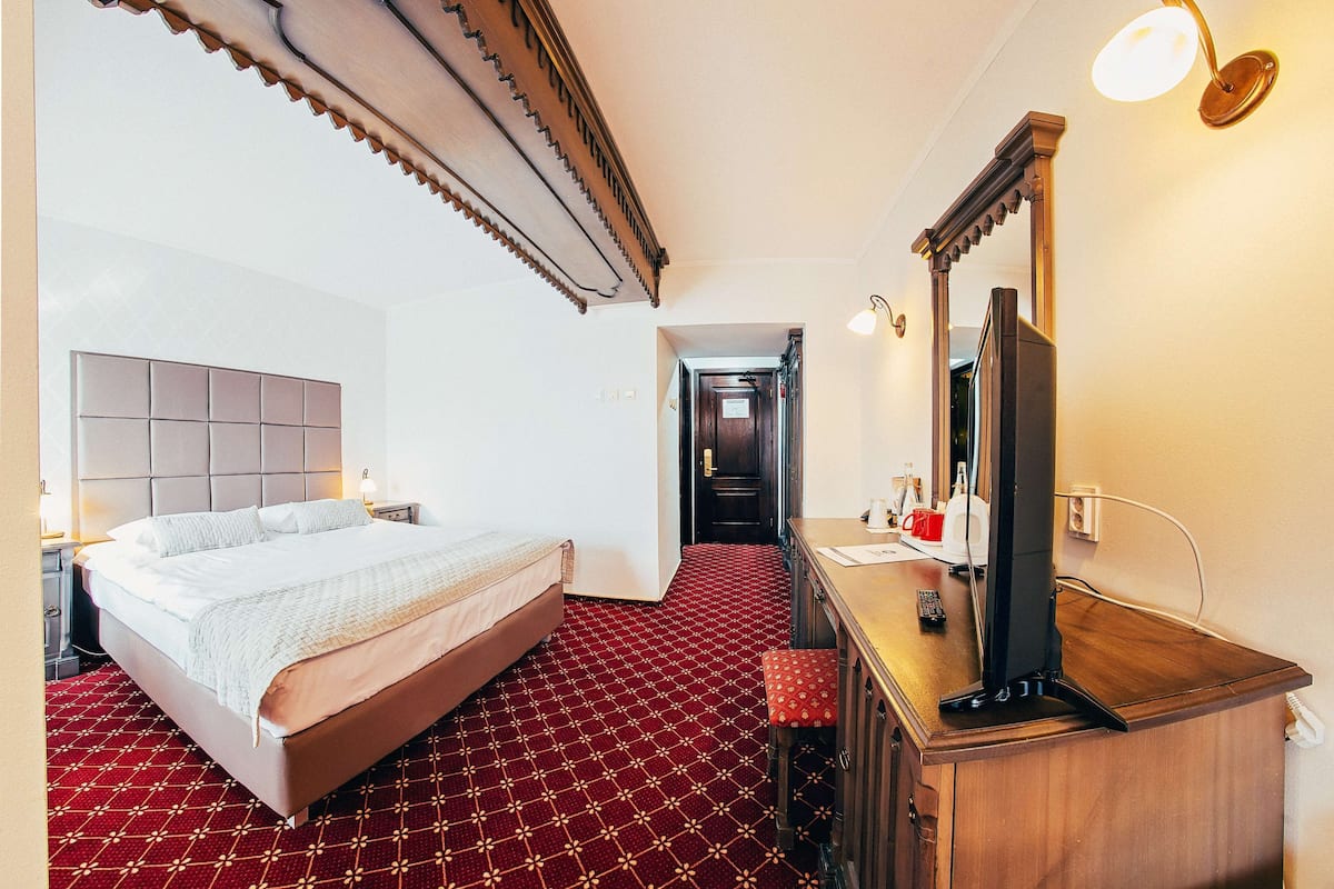 Une chambre d’hôtel avec un grand lit, un bureau en bois, un miroir et une moquette rouge à motifs.