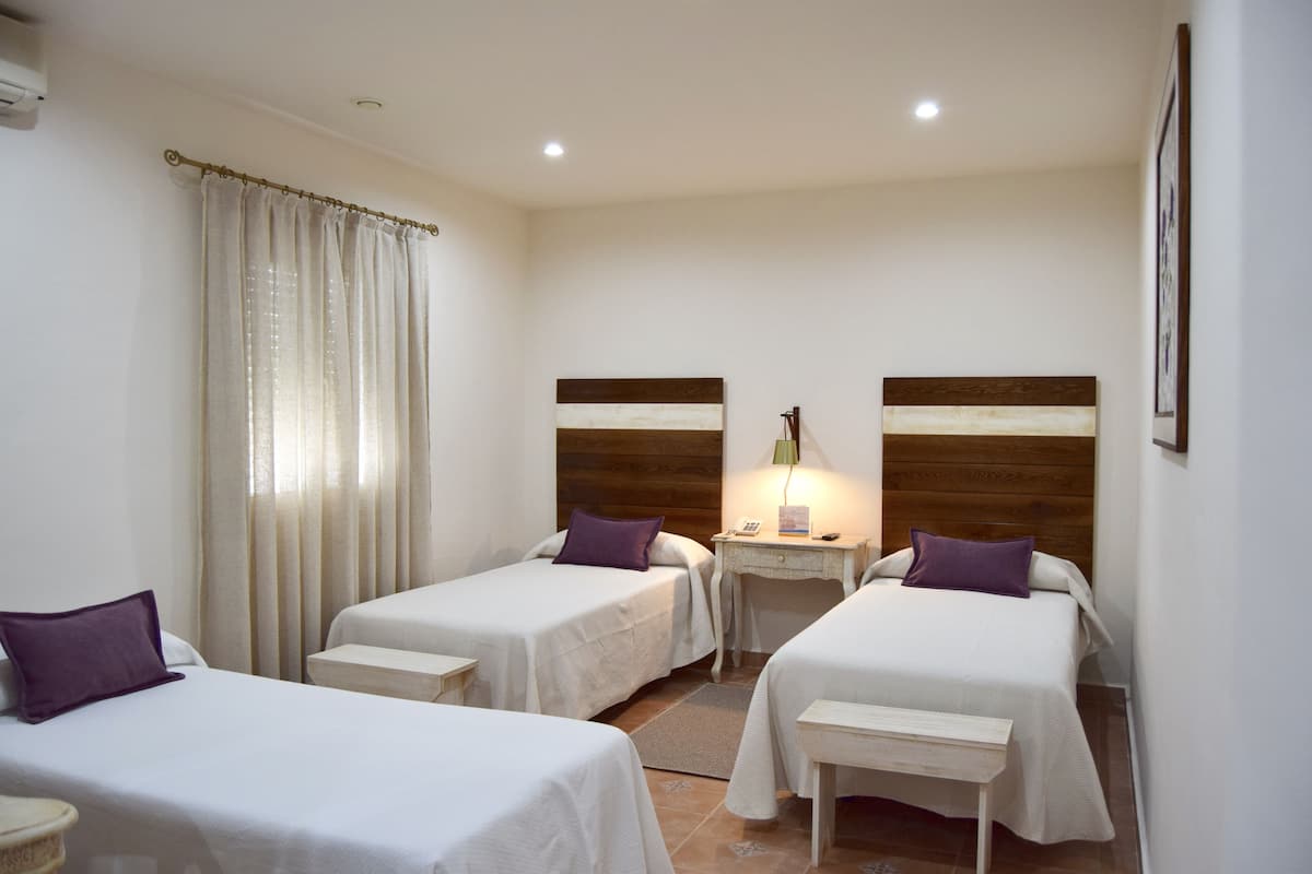 A hotel room with two single beds, a small desk, a nightstand, and a wall-mounted lamp.