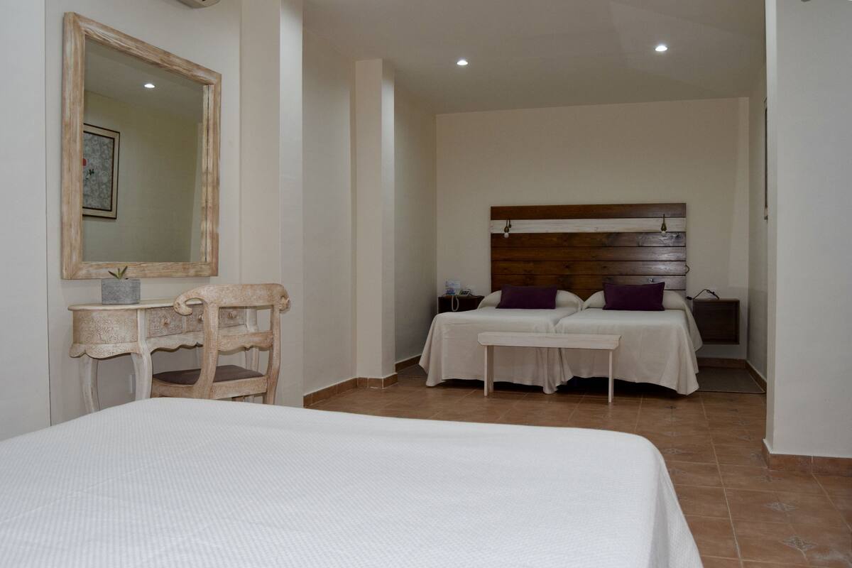 A bedroom with a large bed, a smaller bed, a desk, and a mirror.
