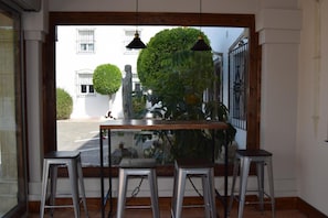 A bar area with a glass partition, three metal stools, and hanging pendant lights. - Hotel Puerta de Algadir (El Puerto de Santa Maria)