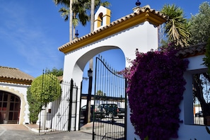 A white building with a large arched entrance, a black gate, and a vehicle parked inside. - Hotel Puerta de Algadir (El Puerto de Santa Maria)