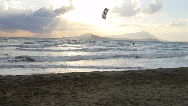 Una playa con olas y un kitesurfista a lo lejos.