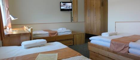 A hotel room with two beds, a desk with a lamp, a TV mounted on the wall, and wooden wardrobes.