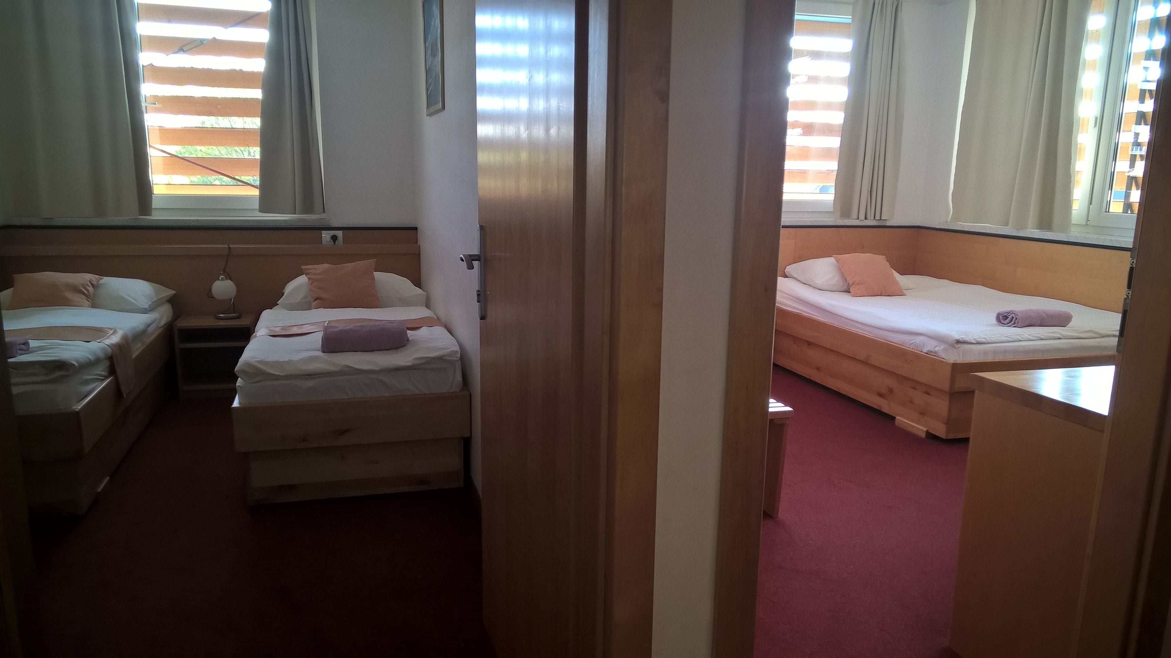 Een hotelkamer met twee bedden, een bureau en een raam met zonwering.