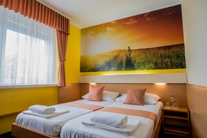 Habitación de hotel con dos camas, un cuadro grande de una puesta de sol y una ventana con cortinas.