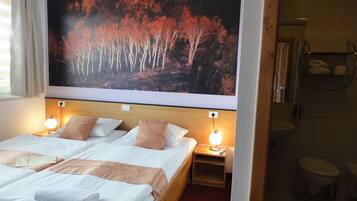 Een hotelkamer met een groot bed, twee nachtkastjes met lampen, een badkamer met douche en een groot wandschilderij.