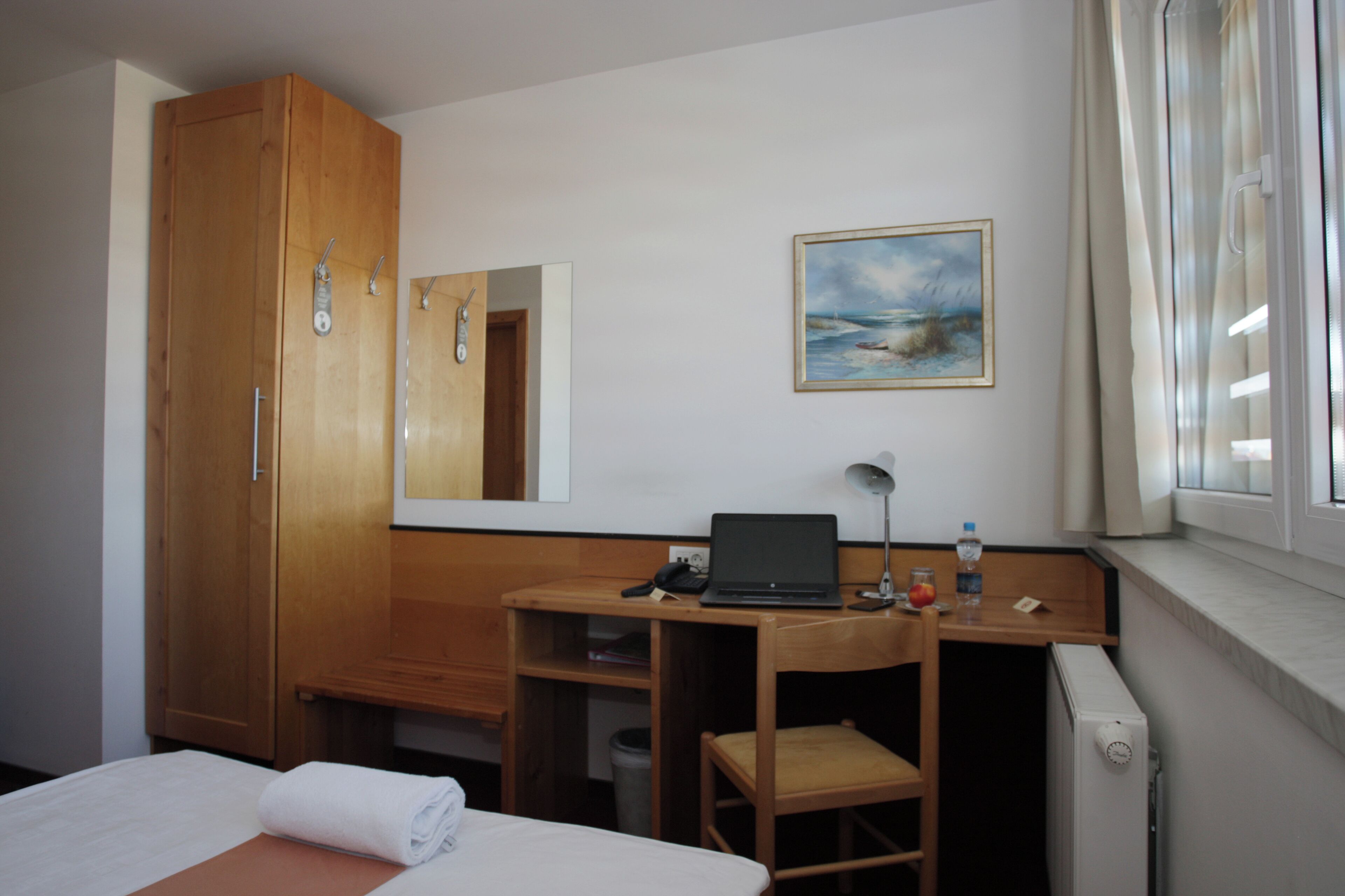 Habitación de hotel con cama, armario de madera, escritorio con una computadora portátil, silla y un cuadro en la pared.