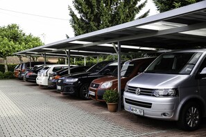 Vários carros estacionados sob uma cobertura, em um terreno pavimentado.