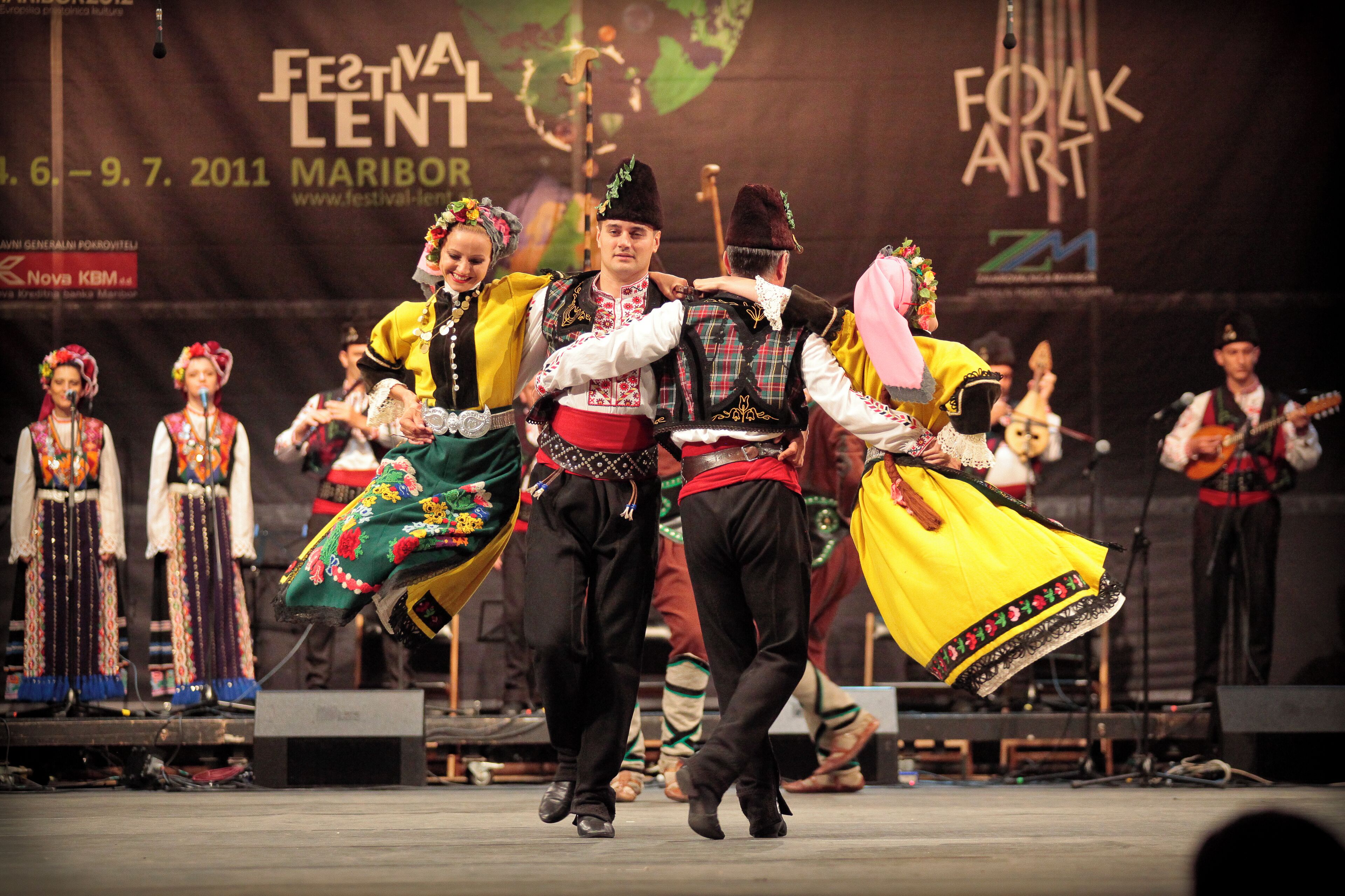 Escenari amb intèrprets amb vestimentes tradicionals, una pancarta amb el text "Festival Lent Maribor" i un logotip de "Folk Art".