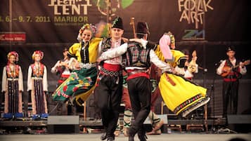 Escenari amb intèrprets amb vestimentes tradicionals, una pancarta amb el text "Festival Lent Maribor" i un logotip de "Folk Art".