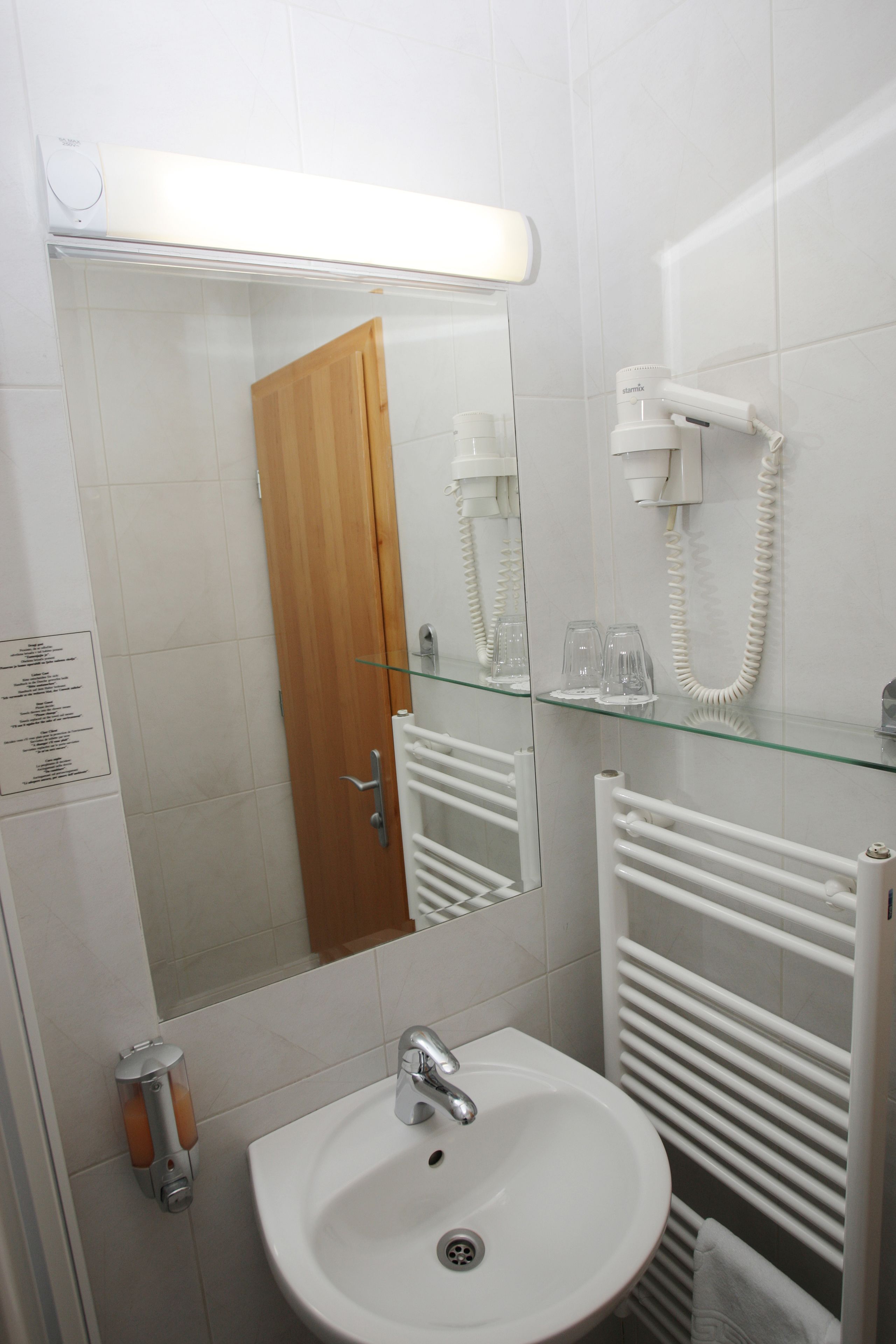 A bathroom with a white sink, a mirror, a glass shelf with glasses, a towel rack, and a heater.