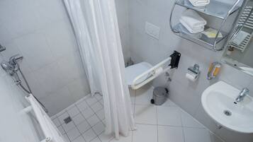 A small bathroom with a shower, toilet, sink, and a shelf with towels.