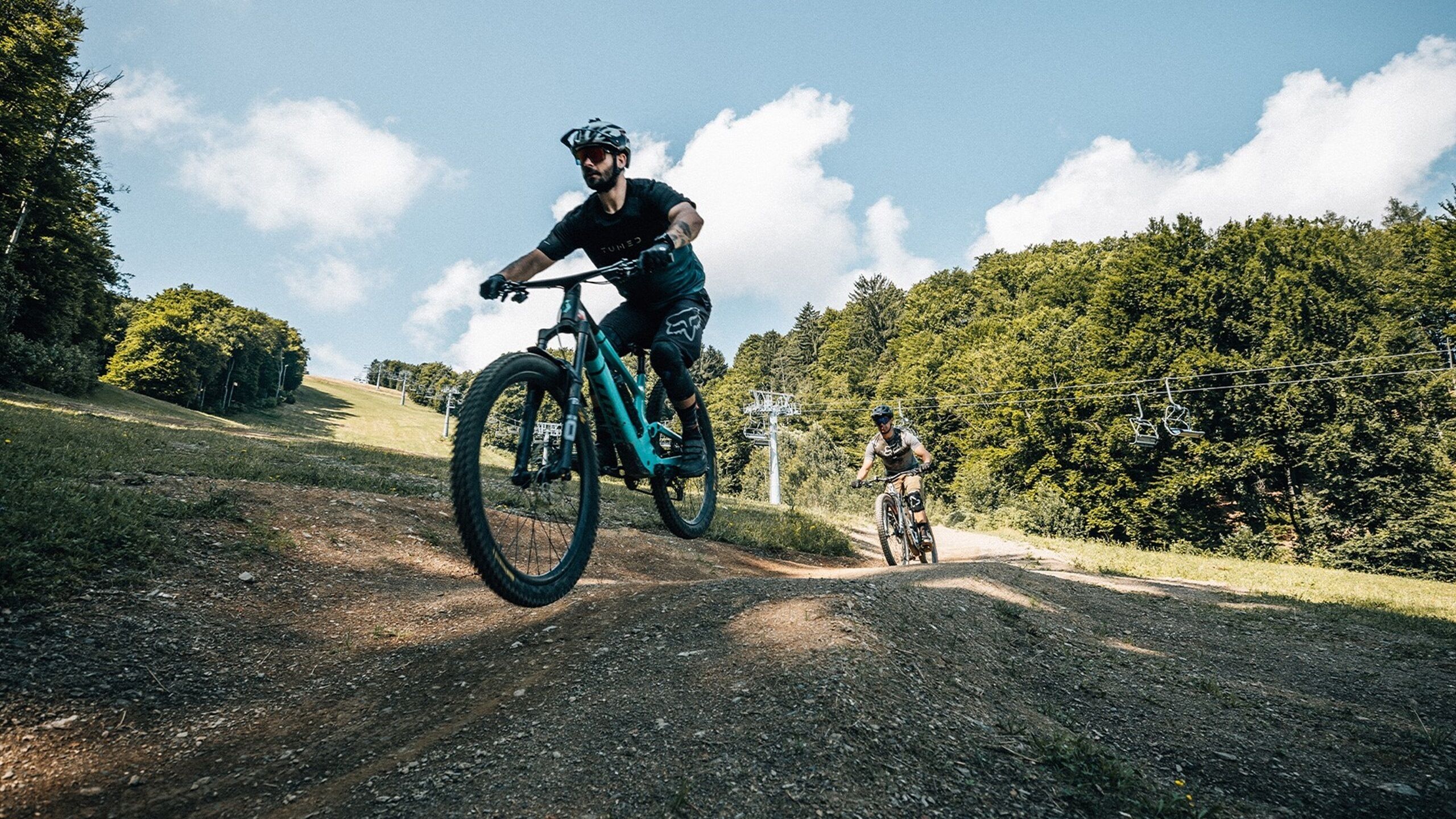 Un sendero de tierra con dos ciclistas, uno en primer plano y otro al fondo.