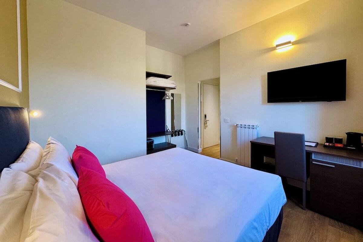 A hotel room with a bed, a desk, a chair, a TV, and a wardrobe.