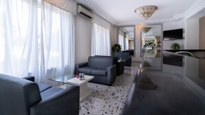 Una habitación de hotel moderna con sofá, sillones, una mesita y televisor.
