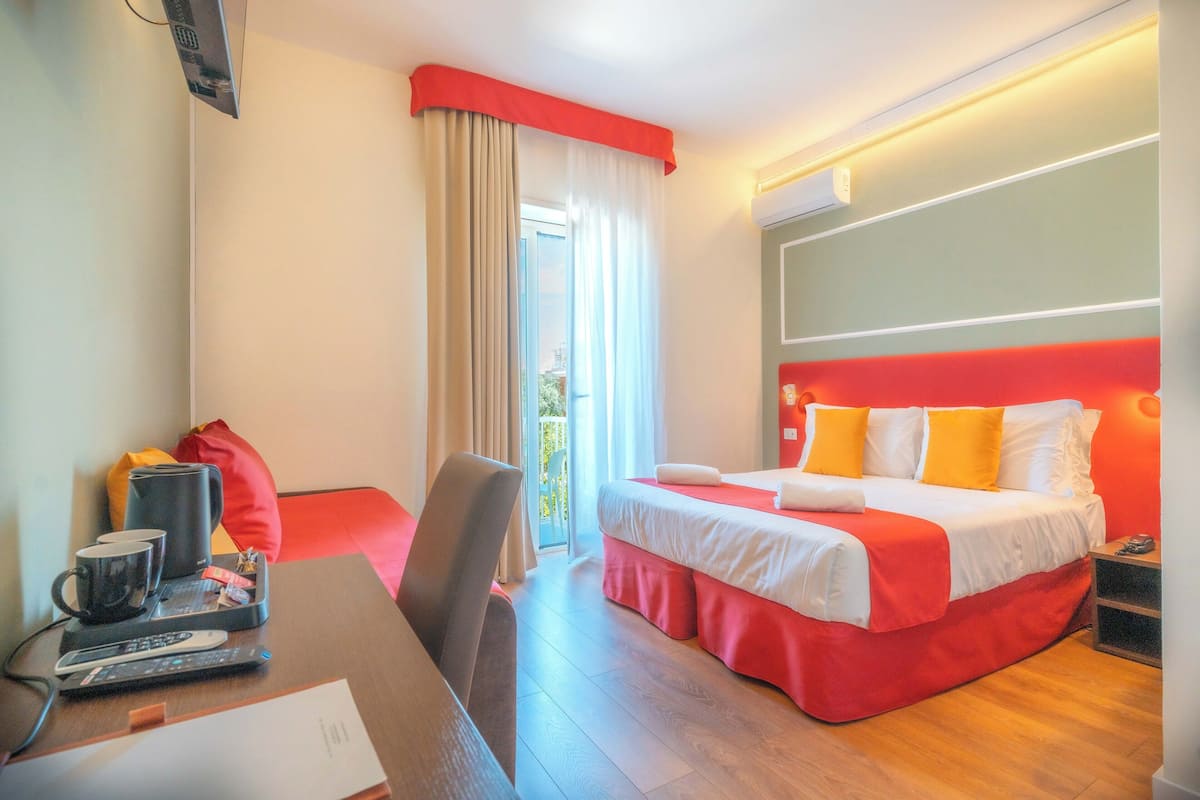A hotel room with a bed, a desk with a chair, a coffee maker, and a TV.
