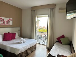 Una camera d'albergo con un letto, un letto aggiuntivo, un balcone con tavolo e sedie e un quadro appeso al muro.