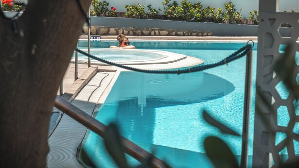 Una piscina con una persona relajándose en el agua, rodeada de una zona de borde de piscina con una barrera de cuerda.