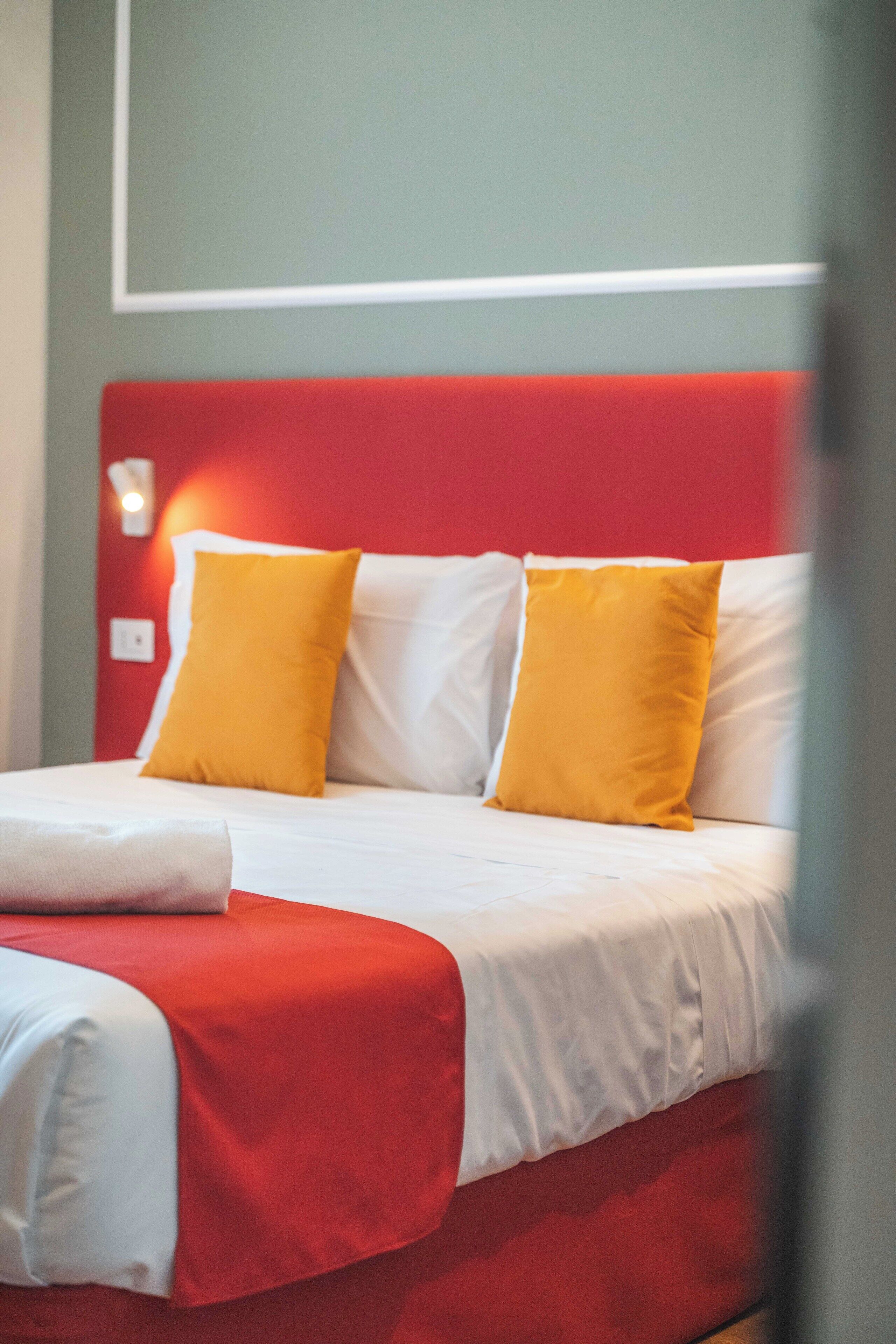A bed with a red headboard and white bedding, two yellow pillows, and a white blanket.