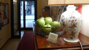 A hallway with a wooden reception desk, a lamp, a vase, and a bowl of green apples. - Albergo Atlantic (Bologna)
