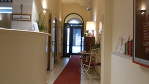 A hotel lobby with a reception desk, a red carpet, a seating area with a table and chairs, and a framed informational poster on the wall. - Albergo Atlantic (Bologna)