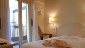 A hotel room with a bed, a nightstand, a wall-mounted lamp, a sliding glass door to a balcony, and a small table. - Albergo Atlantic (Bologna)