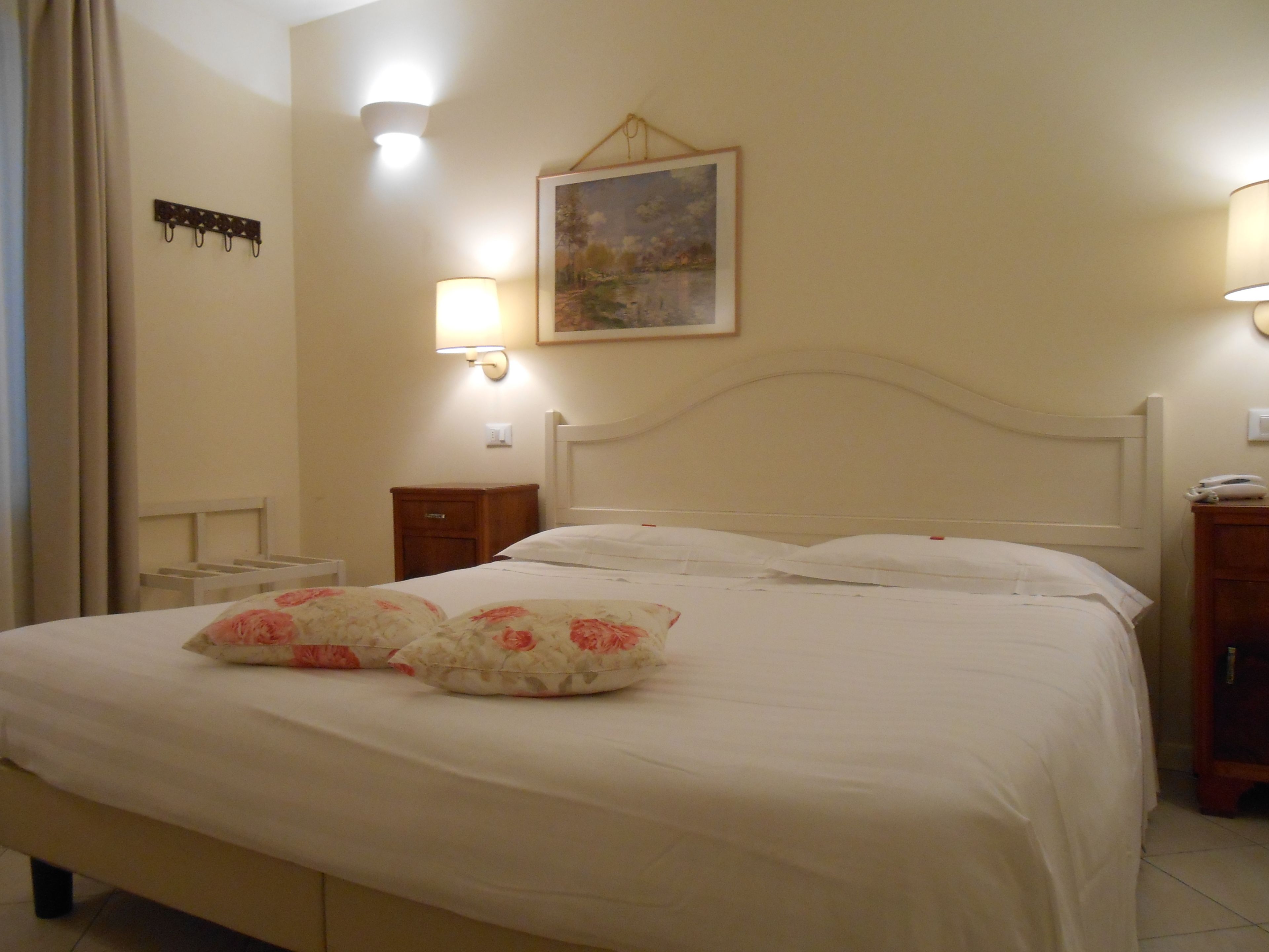 A neatly made bed with floral pillows, a painting on the wall, and bedside lamps.