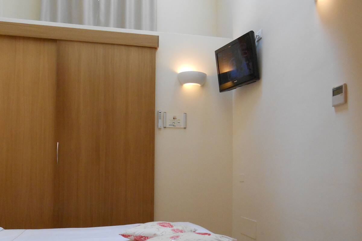 A bedroom with a bed, a television mounted on the wall, and a light fixture above the bed.