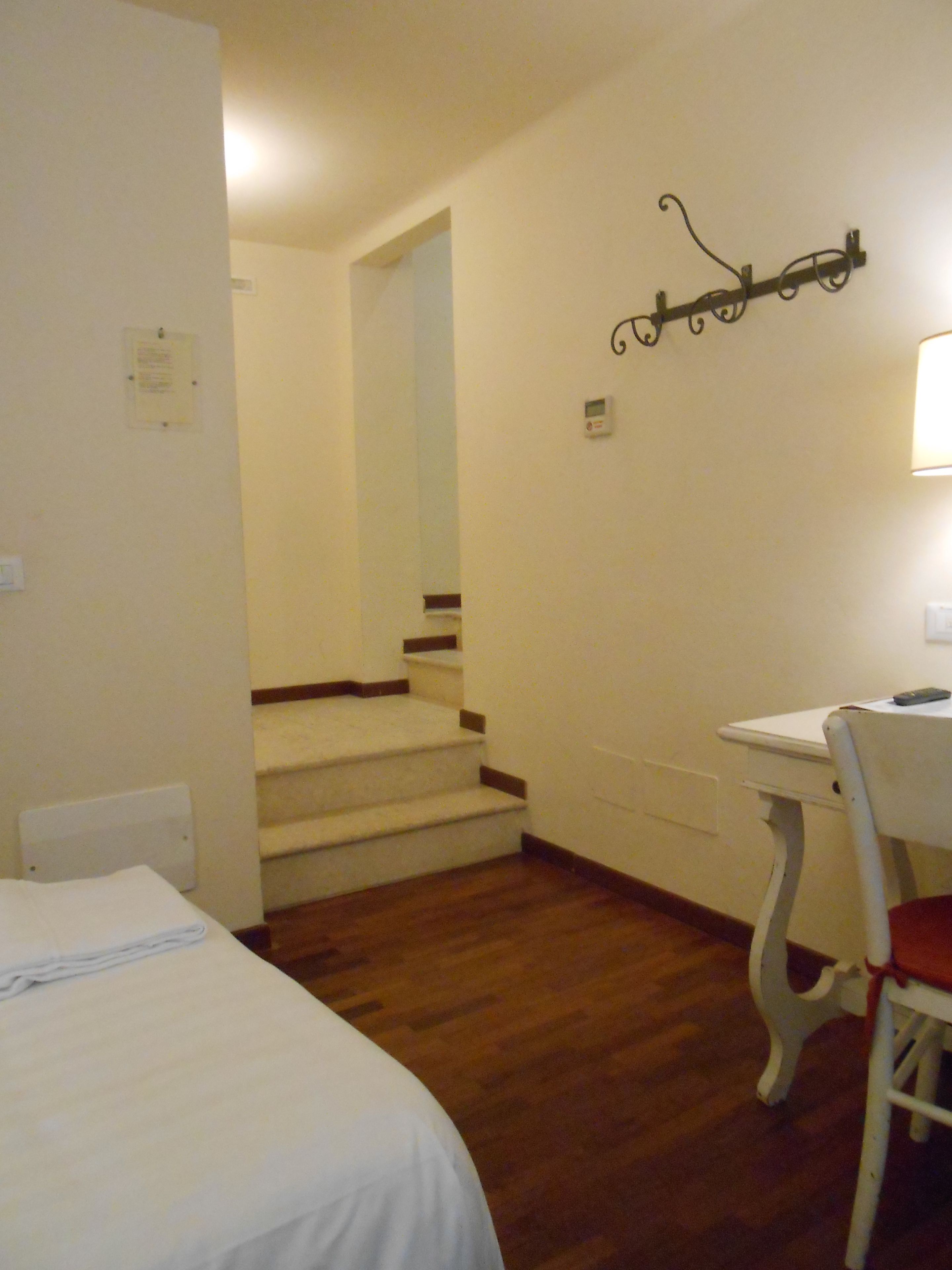 A hotel room with a bed, a desk with a chair, a staircase, and a wall-mounted light fixture.