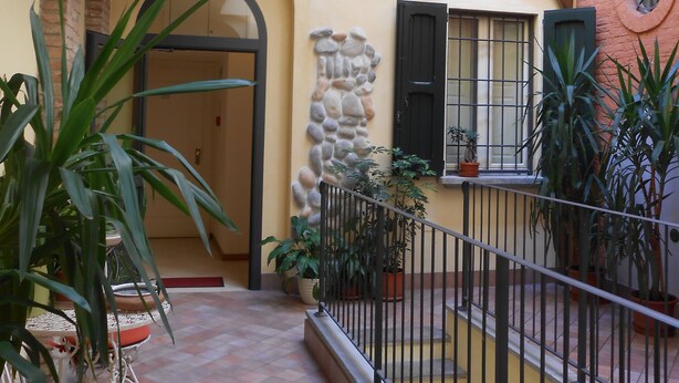 A covered outdoor area with a tiled floor, potted plants, and a metal railing. - Albergo Atlantic (Bologna)