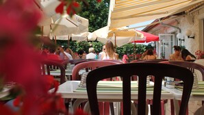 Un área de comedor al aire libre con mesas, sillas, sombrillas y un muro de piedra al fondo.